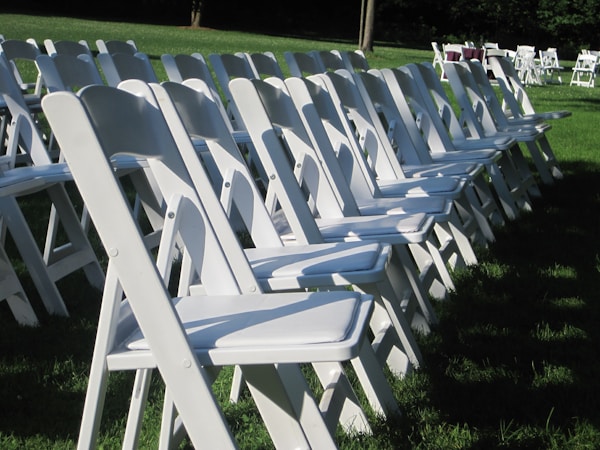 White resin chairs set up for outdoor wedding ceremony — Gulf Coast Event Rentals